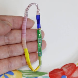 Pu&ograve; includere: Un braccialetto multi-colore con perline rosa, gialle, verdi e blu. Il braccialetto &egrave; fatto di piccole perline quadrate.
