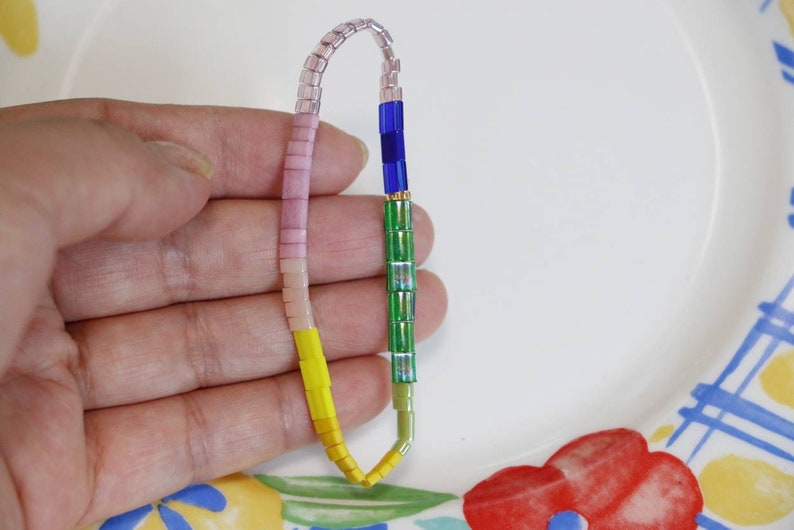 Pu&ograve; includere: Un braccialetto multi-colore con perline rosa, gialle, verdi e blu. Il braccialetto &egrave; fatto di piccole perline quadrate.