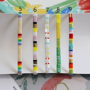 Pu&ograve; includere: Un set di dieci braccialetti in piastrelle colorate, ognuno con un motivo diverso. I braccialetti sono numerati da 5 a 9, e ognuno ha una combinazione di colori diversa. I braccialetti sono fatti di piccole piastrelle quadrate che sono infilate su una corda.