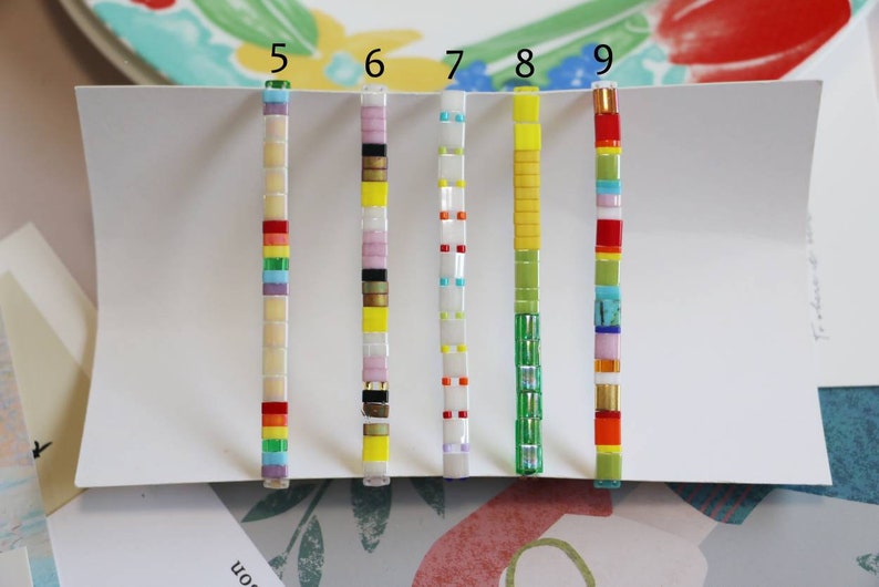 Pu&ograve; includere: Un set di dieci braccialetti in piastrelle colorate, ognuno con un motivo diverso. I braccialetti sono numerati da 5 a 9, e ognuno ha una combinazione di colori diversa. I braccialetti sono fatti di piccole piastrelle quadrate che sono infilate su una corda.