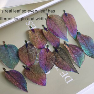 May include: A collection of iridescent, real leaf charms in various shades of purple, blue, and green. The leaves are delicate and have a shimmery finish.