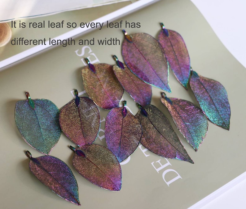 May include: A collection of iridescent, real leaf charms in various shades of purple, blue, and green. The leaves are delicate and have a shimmery finish.