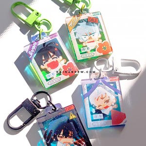 Könnte beinhalten: Vier rechteckige Acryl-Schlüsselanhänger mit Anime-Charakter-Illustrationen. Jeder Anhänger hat einen farbigen Metall-Karabinerverschluss und zeigt den Text RAINUBREW.COM. Die Designs enthalten leuchtende Farben, kleine grafische Details und Barcodes.
