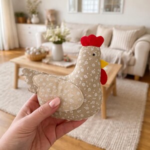 Small fabric Easter chicken plush held in hand showing 5.3 inch size scale in cozy farmhouse living room setting.