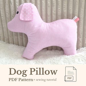 May include: A pink dog-shaped pillow with a gingham pattern and a polka-dot ear. The pillow has a small tail with a patterned tip. The text "Dog Pillow" is displayed below the pillow, along with "PDF Pattern + sewing tutorial".