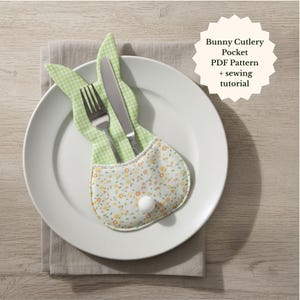 May include: A white plate with a bunny-shaped cutlery pocket holding a fork and knife. The pocket is green gingham and floral fabric with a white pom-pom tail. Text on the image reads "Bunny Cutlery Pocket PDF Pattern + sewing tutorial."