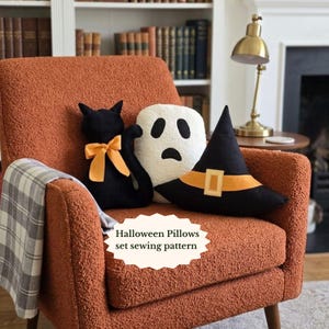 May include: A set of three decorative cushions featuring a black cat with an orange bow, a white ghost with black facial features, and a black witch hat with an orange band and buckle. The text "Halloween Pillows set sewing pattern" is visible.