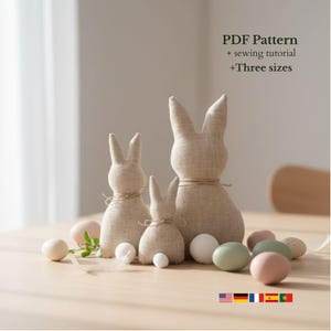 May include: Three beige fabric bunny figures of varying sizes, tied with twine, are displayed on a light wooden surface. The image includes pastel-colored Easter eggs and the text "PDF Pattern + sewing tutorial +Three sizes".