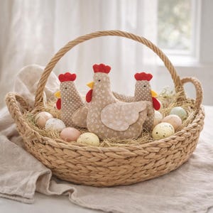 May include: A woven basket filled with three fabric chickens, speckled eggs, and straw. The chickens have red combs, yellow beaks, and patterned bodies. The basket has a woven handle and sits on a neutral-colored cloth.