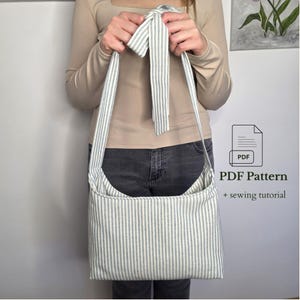 May include: A white and grey striped shoulder bag with a long strap. The bag's strap is tied at the top. The image shows the text "PDF Pattern + sewing tutorial". The bag is made of fabric.