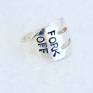 May include: A silver ring with the words "Fork Off" engraved on it.