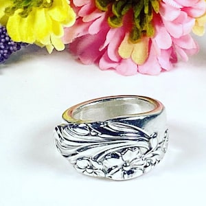 May include: A silver ring made from a repurposed spoon with a floral design. The ring is wide and has a detailed floral pattern.