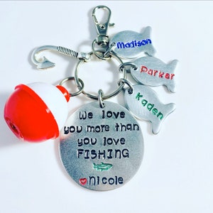 May include: A silver keychain with a red and white bobber, a silver hook, and four silver fish charms. The fish charms have the names "Madison", "Parker", "Kaden", and "Nicole" engraved on them. The main charm has the text "We love you more than you love FISHING".