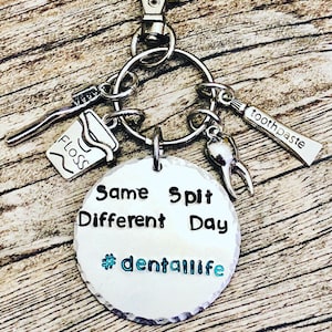 May include: Silver keychain with dental-themed charms, including a toothbrush, floss, toothpaste tube, and a tooth. A round charm features the text "Same Spit Different Day" and "#dentallife".