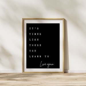 Puede incluir: Una impresión enmarcada en blanco y negro con el texto "It's times like these you learn to live again" en un estilo de fuente minimalista.
