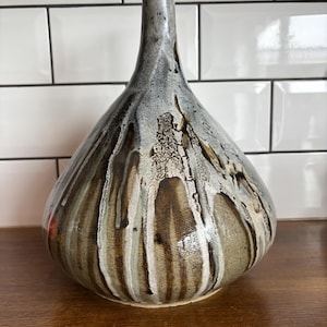 May include: A ceramic vase with a distinctive teardrop form and a slender neck. The vase has a textured finish with a mix of brown, grey, and white glaze, producing a drip effect. A decorative item for the home.