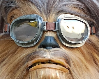 May include: A person wearing a brown and grey furry costume with a pair of silver aviator goggles.
