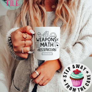 May include: White ceramic mug with the text "WEAPONS of MATH DESTRUCTION" and math-related graphics. The mug also has a ruler, calculator, protractor, and playing cards. A sticker with a cupcake and the text "STEP AWAY FROM THE CAKE" is also visible.