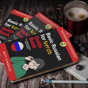 Puede incluir: Tres ejemplares de "Basic Russian for Nerds Guide Book" con una bandera rusa y una ilustraci&oacute;n de dibujos animados. Una taza de caf&eacute;, ar&aacute;ndanos, un bol&iacute;grafo y un peque&ntilde;o cuaderno est&aacute;n sobre una superficie de madera.