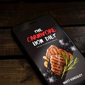 Puede incluir: Un tel&eacute;fono inteligente que muestra la portada de un libro con el t&iacute;tulo "The Carnivore Lion Diet: The Key to Optimum Health" en texto rojo y blanco. La portada presenta un primer plano de carne a la parrilla con romero y ajo sobre un fondo negro.