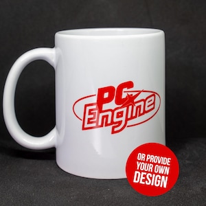 May include: A white ceramic mug featuring the red text PC Engine inside a red oval graphic. A circular red badge in the lower right corner contains the white text OR PROVIDE YOUR OWN DESIGN. The mug has a curved handle on the left side.