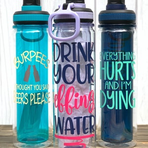 K&ouml;nnte beinhalten: Drei durchsichtige Wasserflaschen aus Plastik mit verschiedenen motivierenden Spr&uuml;chen. Die erste Flasche ist t&uuml;rkisblau mit goldenen Buchstaben, auf denen "Burpees Thought You Said Beers Please" steht. Die zweite Flasche ist klar mit violetten Akzenten und tr&auml;gt die Aufschrift "Drink Your Effing Water" in dunkelblau und rosa Schrift. Die dritte Flasche ist dunkelblau mit t&uuml;rkisfarbener Schrift, auf der "Everything Hurts And I'm Dying" steht.