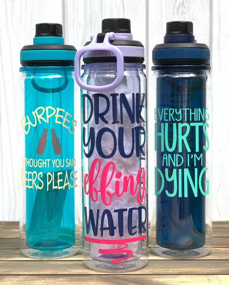 K&ouml;nnte beinhalten: Drei durchsichtige Wasserflaschen aus Plastik mit verschiedenen motivierenden Spr&uuml;chen. Die erste Flasche ist t&uuml;rkisblau mit goldenen Buchstaben, auf denen "Burpees Thought You Said Beers Please" steht. Die zweite Flasche ist klar mit violetten Akzenten und tr&auml;gt die Aufschrift "Drink Your Effing Water" in dunkelblau und rosa Schrift. Die dritte Flasche ist dunkelblau mit t&uuml;rkisfarbener Schrift, auf der "Everything Hurts And I'm Dying" steht.