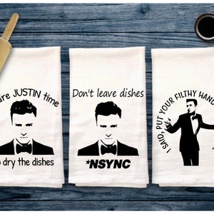 May include: Set of three white kitchen towels with black text and images. The first towel says "You're JUSTIN time to dry the dishes" and features a black and white image of Justin Timberlake. The second towel says "Don't leave dishes *NSYNC" and features a black and white image of Justin Timberlake. The third towel says "I SAID, PUT YOUR FILTHY HANDS ALL OVER ME" and features a black and white image of Justin Timberlake.
