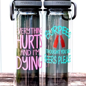 K&ouml;nnte beinhalten: Zwei durchsichtige Wasserflaschen aus Plastik mit schwarzen Deckeln und Tragegriffen. Die linke Flasche tr&auml;gt den Text "Everything Hurts and I'm Dying" in rosa Schrift. Die rechte Flasche tr&auml;gt den Text "Burpees I Thought You Said Beers Please" in t&uuml;rkisfarbener Schrift mit einer roten Grafik von zwei Bierflaschen.