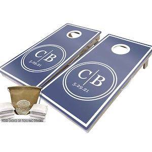 May include: A set of two blue cornhole boards with white trim and a white circle with the initials "C|B" and the date "5.29.21". The set includes a brown canvas bag with white drawstring and eight white bean bags.
