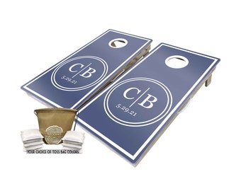 May include: A set of two blue cornhole boards with white trim and a white circle with the initials "C|B" and the date "5.29.21". The set includes a brown canvas bag with white drawstring and eight white bean bags.