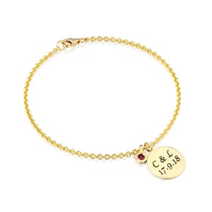 May include: Gold chain bracelet with a round charm engraved with "C & L 17.9.18" and a small red gemstone.