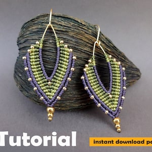 Puede incluir: Un par de pendientes de macramé verde y morado con cuentas doradas. Los pendientes tienen forma de V y cuelgan de ganchos dorados. Los pendientes están sobre una superficie de madera. Tutorial descarga instantánea pdf.