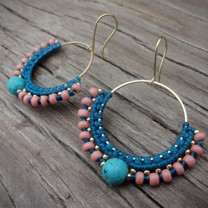 May include: A pair of gold hoop earrings with turquoise and pink beads. The earrings are handmade and feature a unique macrame design.