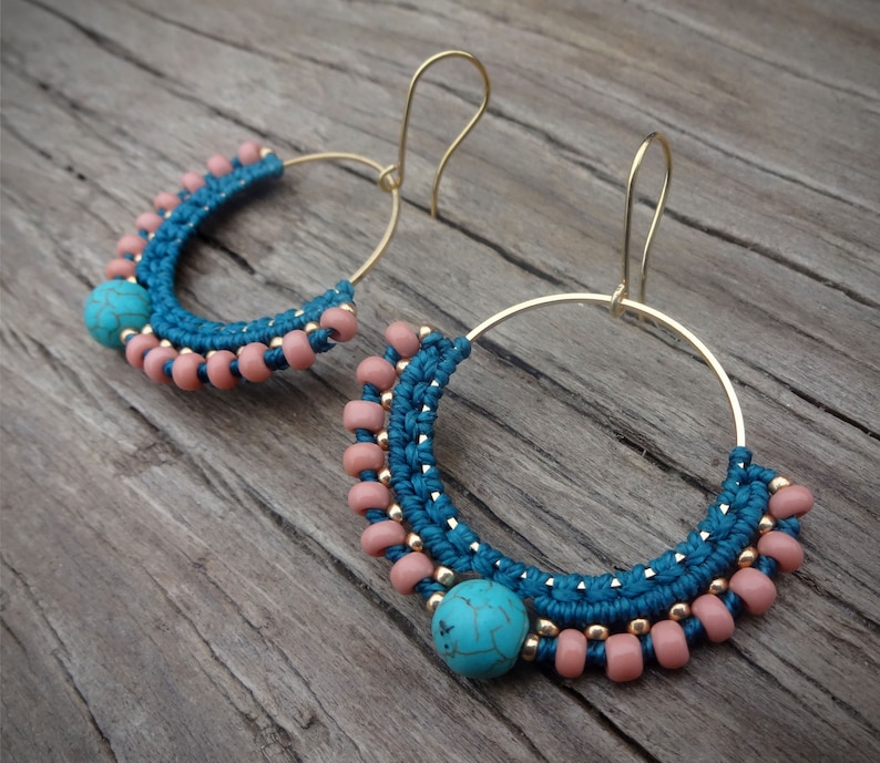 May include: A pair of gold hoop earrings with turquoise and pink beads. The earrings are handmade and feature a unique macrame design.