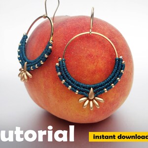 May include: A pair of gold hoop earrings with a teal blue macrame design and a gold starburst charm. The earrings are displayed on a peach.