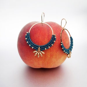 May include: A pair of gold hoop earrings with a teal blue woven design and a gold flower charm.
