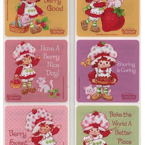 May include: A collection of six Strawberry Shortcake stickers. Each sticker shows a cartoon girl with red hair and a strawberry hat. The stickers have phrases such as "Berry Good" and "Bake the World A Better Place".