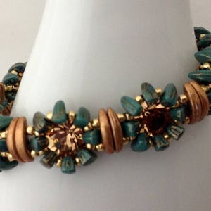 May include: A teal and copper beaded bracelet with a flower design. The bracelet is made with small, round beads and has a delicate, feminine look.