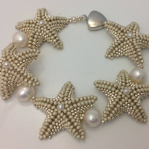 May include: A bracelet made of beige beads in the shape of starfish, with white pearls interspersed throughout. The bracelet has a silver heart-shaped clasp.