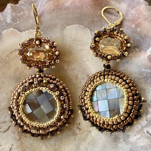 May include: A pair of gold and brown beaded earrings with a large round shell and a smaller oval crystal. The earrings are dangling and have a hook closure.