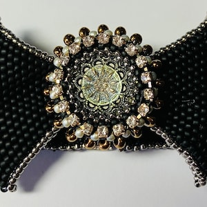 May include: A black beaded bow with a silver and gold embellished center featuring a round, iridescent button.