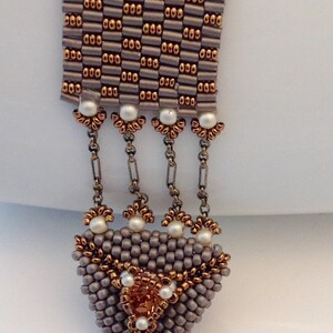 May include: A gray and copper beaded bracelet with a triangular pendant featuring a copper bead in the center. The bracelet has a toggle clasp.