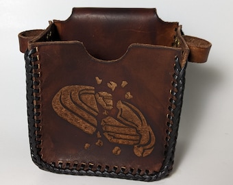 May include: A brown leather box with a black braided trim and a design of a broken heart. The box has a flap top and a handle.