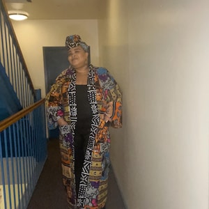 May include: A long, colorful patterned kimono with black trim and a black top underneath. The kimono has a variety of geometric and abstract designs in shades of orange, yellow, blue, purple, and white.