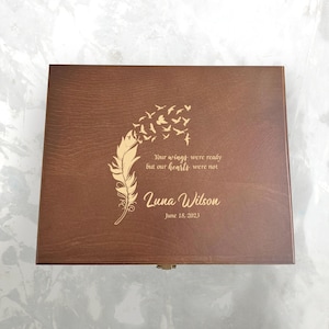 May include: A wooden box with a dark brown finish. The lid features an engraved feather design with flying birds and the text "Your wings were ready but our hearts were not." The name "Luna Wilson" and the date "June 18, 2023" are also engraved.