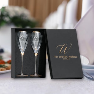 May include: Two champagne flutes with gold rims in a black box. The flutes are engraved with the letter "W" and the text "Mr. and Mrs. Wallace 10.10.18".