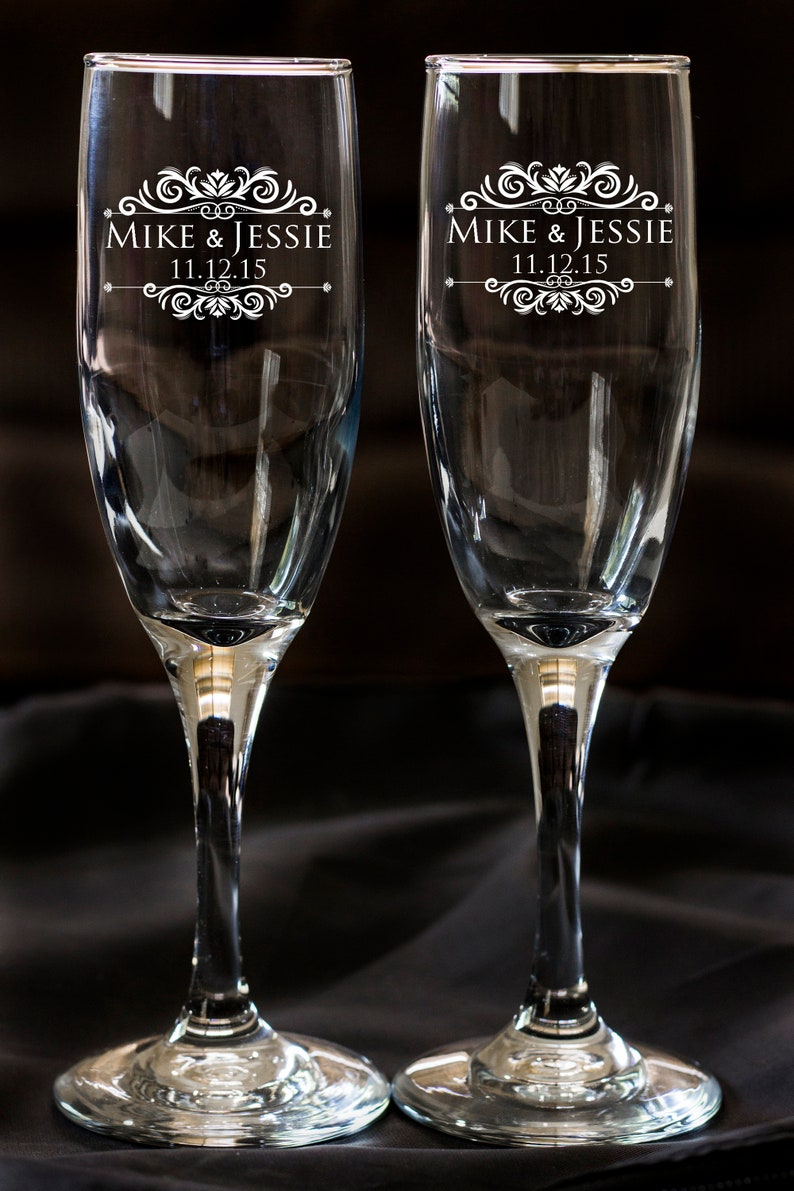 May include: Two clear glass champagne flutes with a decorative design and the text "Mike & Jessie 11.12.15" etched on the front.
