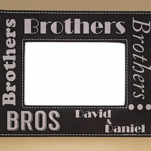 May include: Black leather picture frame with a stitched border. The frame has the words "Brothers" and "Bros" in silver lettering. The bottom of the frame has the names "David & Daniel" in silver lettering.