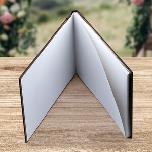 May include: A brown leather-bound journal with blank pages, open to reveal the white paper inside. The journal is lying flat on a wooden surface.